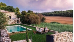 A stone building with a pool and a dining area with people.