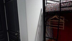 A bunk bed with a patterned pillow, a wooden hanger, and a chair in a room with a red wall and a white door. - Mini gîte, studette  (Bonny-sur-Loire)