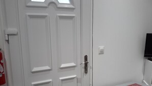 A white door with a handle and a small window above it. There is a white table with a red and white tablecloth to the right of the door. - Mini gîte, studette  (Bonny-sur-Loire)