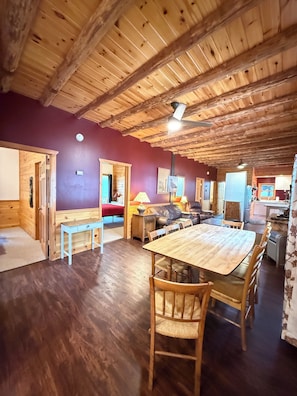 A wooden interior with a dining table, chairs, a sofa, and a kitchen area.
