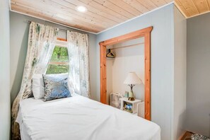 A bedroom with a bed, a window with curtains, a bedside table with a lamp, and a wooden headboard.