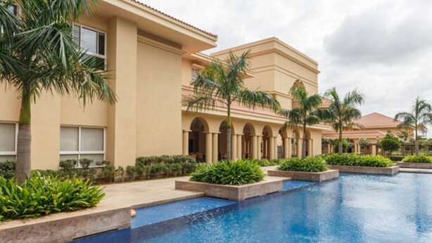 A resort with a large pool, palm trees, and a building with arched windows. - Close to Airport and Manyata Tech Park |  25% Off for Long Stays (BENGALURU)