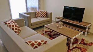 A living room with a sofa, armchair, coffee table, and a TV on a stand. - Close to Airport and Manyata Tech Park |  25% Off for Long Stays (BENGALURU)