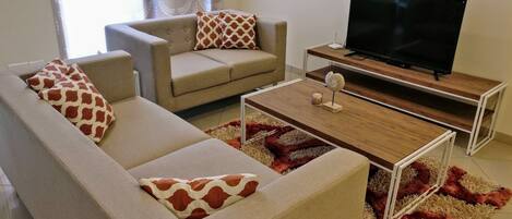 A living room with a sofa, armchair, coffee table, and a TV on a stand.