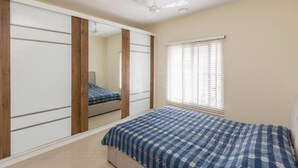 A bedroom with a bed, a window with blinds, a ceiling fan, and a wardrobe with a mirror. - Close to Airport and Manyata Tech Park |  25% Off for Long Stays (BENGALURU)