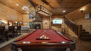 A pool table with billiard balls, a fireplace, a television, and a staircase.