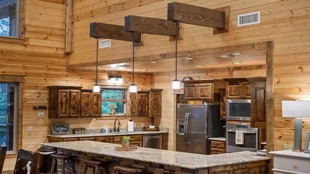 Eine geräumige Küche mit Holzwänden, Granit Arbeitsplatten und Edelstahlgeräten, ausgestattet mit Pendelleuchten.