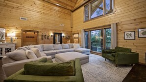 Ein geräumiges Wohnzimmer mit einer großen Eckcouch, einem grünen Sessel und einer Glastür, die auf einen Balkon führt.