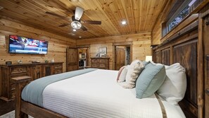 Ein Schlafzimmer einer Holzh ütte mit Bett, Deckenventilator, Fernseher und Kommode.