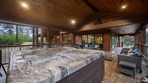 Eine Holzterrasse mit Whirlpool, Sitzgelegenheiten im Freien und großen Fenstern mit Blick auf eine natürliche Landschaft.
