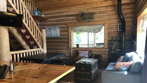 A cozy cabin interior with a wooden staircase, a fireplace, a sofa, and a bar area.