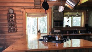 A wooden cabin kitchen with a large island, a stove, a kettle, and a hanging pot rack.