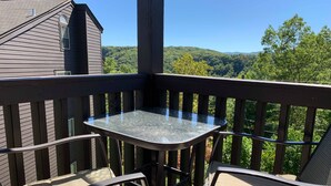 A balcony with a small table and two chairs, overlooking a forested landscape. - Baby Bear HideAway (Gatlinburg)