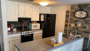 A kitchen with white cabinets, a black refrigerator, a microwave, a stove, and a sink. - Baby Bear HideAway (Gatlinburg)
