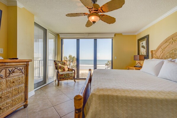 A bedroom with a large bed, a chair, a ceiling fan, and a view of the beach. - Unsurpassed Oceanfront Beauty (Crescent Beach)