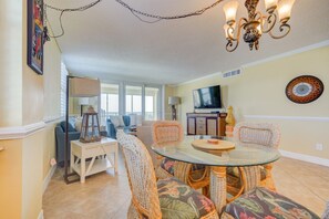 A dining area with wicker chairs and a glass table, a television, and a decorative wall clock. - Unsurpassed Oceanfront Beauty (Crescent Beach)