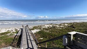 Un paseo marítimo de madera que lleva a una playa con dunas y vegetación.