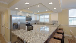 Una cocina moderna con encimeras de granito, electrodomésticos de acero inoxidable y una barra de desayuno con taburetes de mimbre.