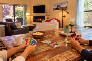 Ein gemütliches Interieur mit einem Holztisch, einer Popcornschale, einer Tasse, Spielkarten und einem Weinglas.