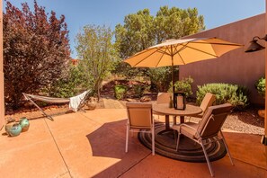 Eine Terrasse im Freien mit einem runden Tisch, zwei Stühlen, einer Hängematte und einem großen Sonnenschirm.