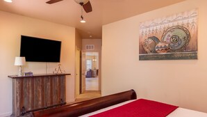 Un dormitorio con cama, ventilador de techo, televisión y un cuadro en la pared.