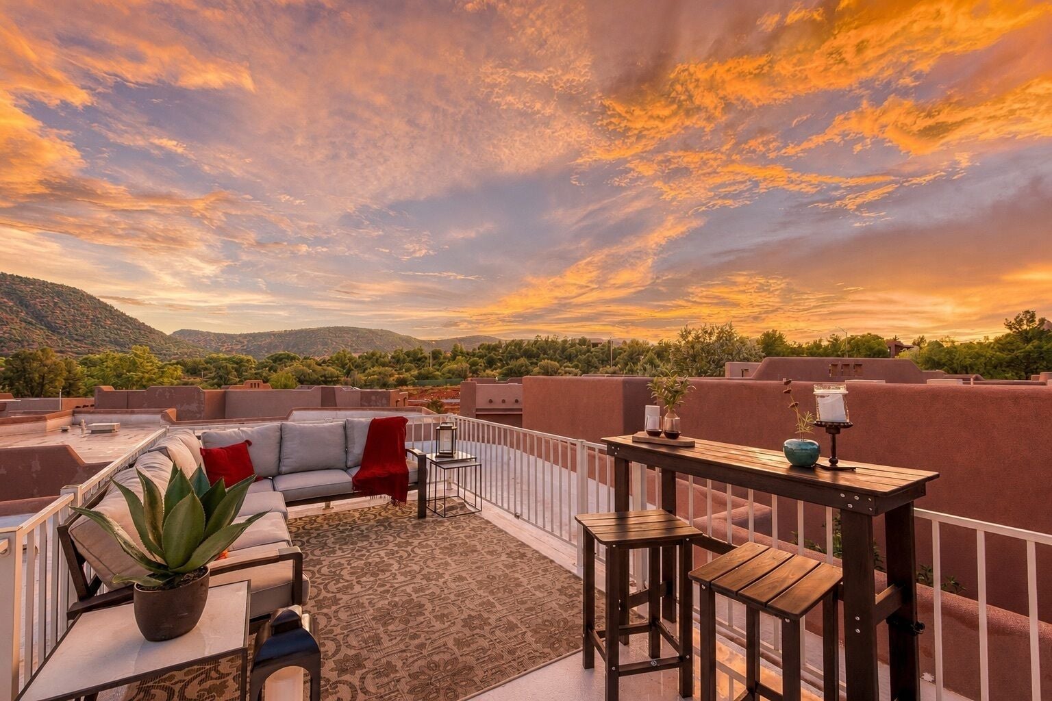 Terraço no telhado com um sofá, cadeiras, uma mesinha e um vaso de planta.