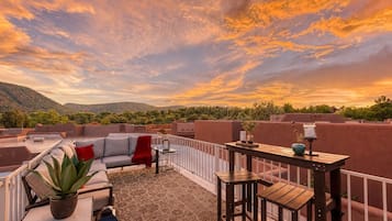 Terraço no telhado com um sofá, cadeiras, uma mesinha e um vaso de planta.