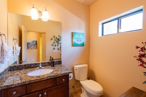 A bathroom with a granite countertop sink, a toilet, and a window.