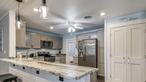 Una cocina moderna con encimera de mármol, electrodomésticos de acero inoxidable e iluminación colgante.