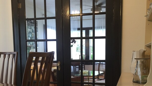 Una habitació amb taula i cadires de fusta, una porta de vidre amb marc negre i un armari blanc.