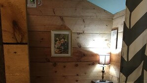 Une petite pièce accueillante avec un plafond en bois, un lit recouvert d’une literie blanche, une lampe de chevet et un tableau encadré accroché au mur.