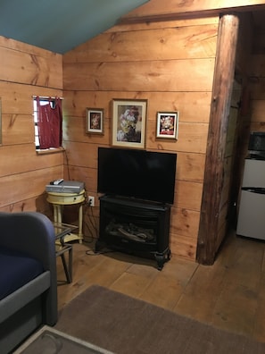Una habitación acogedora con paredes de madera, un televisor, una mesita con un control remoto y fotografías enmarcadas en la pared.