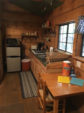 Una cocina compacta con paredes de madera, un microondas, un refrigerador, un lavamanos y una estufa.