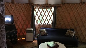 Un intérieur chaleureux avec un canapé bleu foncé, une petite table ronde sur laquelle est posé un jeu d’échecs, un climatiseur blanc et un téléviseur placé sur un meuble en bois.