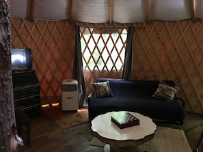 Un ambiente acogedor con un sofá azul oscuro, una pequeña mesa redonda con un tablero de ajedrez, un aire acondicionado blanco y un televisor sobre un mueble de madera.