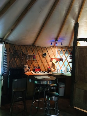 Cocina compacta con techo de madera, cocina a gas, cafetera y taburetes de bar.