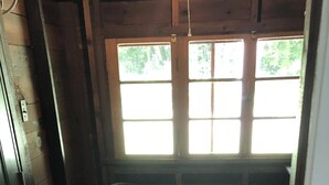Une petite pièce avec un plancher en bois, deux chaises, une petite table et une fenêtre donnant sur des arbres.
