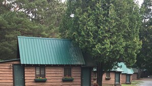 Une rangée de chalets en rondins, avec des toits verts et des portes en bois, s’étend le long d’une allée de gravier.