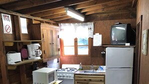 Une cuisine compacte avec des meubles en bois, un four à micro-ondes, une cuisinière, un réfrigérateur et un téléviseur posé sur une étagère.