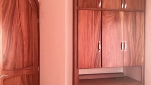 Een slaapkamer met een houten garderobe, een bed met een bloemenbedekking en een betegelde vloer.