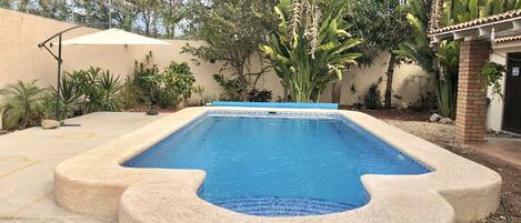 A rectangular swimming pool with a blue mosaic border, surrounded by a beige stone deck.