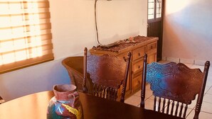 Een eethoek met een houten tafel, stoelen en een decoratieve vaas. Een televisie is aan de muur boven de tafel bevestigd.
