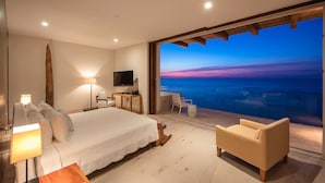 A modern hotel room with a large bed, a desk, a TV, and a balcony with a view of the ocean at sunset. - MODERN AND LUXURY OCEANFRONT VILLA (Puerto Vallarta)