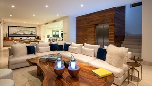 A modern living room with a sectional sofa, a wooden coffee table with two illuminated lamps, and a yellow book on a side table. - MODERN AND LUXURY OCEANFRONT VILLA (Puerto Vallarta)