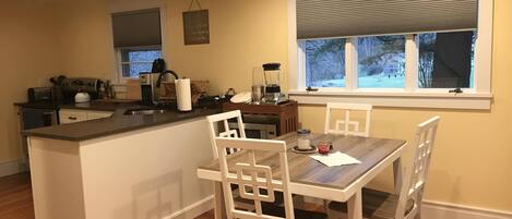 A kitchen with a central island, white chairs, and a window with blinds.