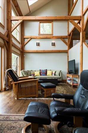 Ein geräumiges Wohnzimmer mit hohen Decken, Holzbalken, einer Sofagarnitur, einem Fernseher und einem Kamin.
