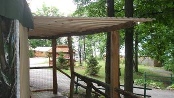 A covered wooden deck with a metal roof, surrounded by trees and a gravel path.