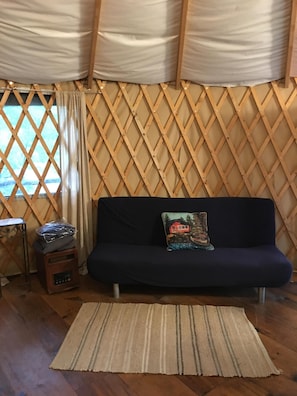 Um quarto com um sofá azul escuro, um tapete estampado, uma pequena mesa de madeira com um rádio e uma parede de madeira gradeada.