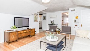 Uma sala de estar ampla com televisão de tela plana, móveis de madeira, uma mesa de centro com objetos decorativos e um espaço de estar aconchegante.