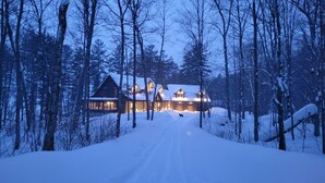 Een besneeuwde pad naar een lodge met meerdere chalets, omringd door bomen.
